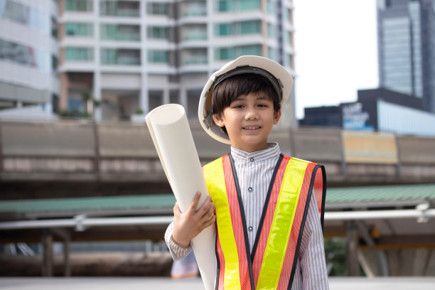 小男孩戴着工程头盔，手里拿着城市建筑图纸。启发孩子未来的理念。图片下载