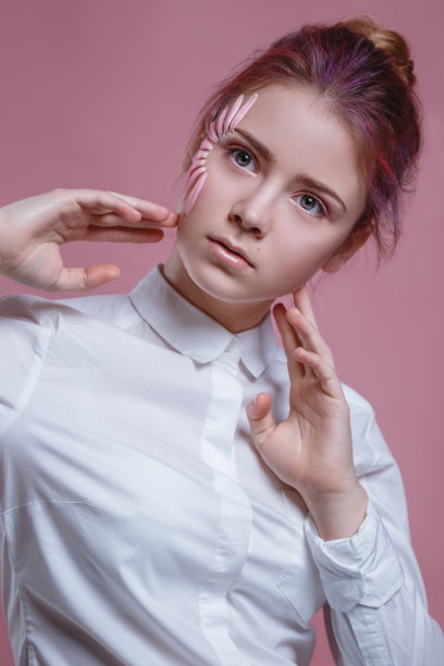 美丽的年轻女子的肖像看着相机与花。近脸美女与花非洲菊在粉红色的背景。护肤美容理念。图片下载