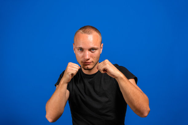 年轻英俊的男子孤立在蓝色的背景下准备用拳头防御的姿势打斗，一脸愤怒和不安，害怕问题图片下载