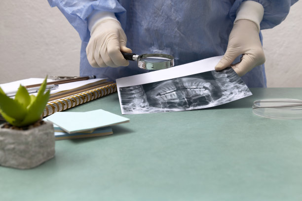 牙医穿着蓝色的实验服，戴着手套，用放大镜分析牙齿x光片。牙科诊所的书桌上。空的空间图片下载