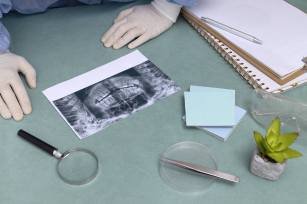 牙科医生办公桌的俯视图。牙齿、镊子、实验碟、放大镜、笔记本、蓝色桌子上的装饰植物。牙医穿着医疗制服，正在分析x光片图片下载