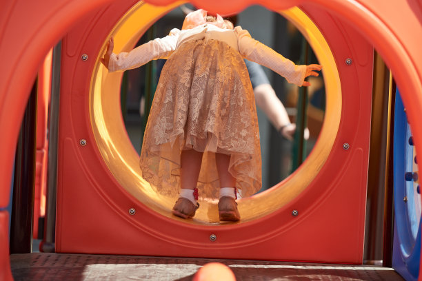 一个穿着裙子的小女孩在儿童塑料滑梯上玩耍图片下载