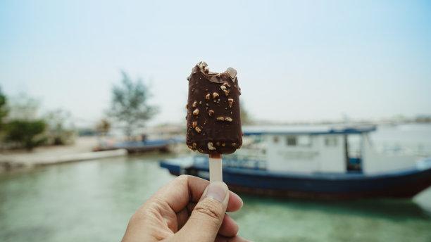 手拿巧克力冰棒在海滩上图片下载