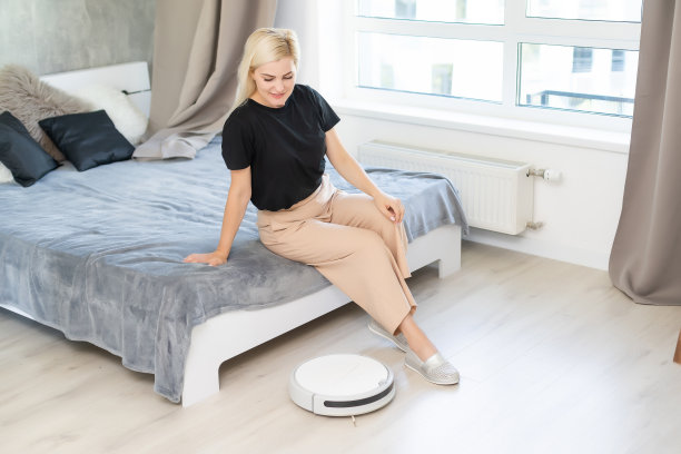 年轻女子用自动吸尘器打扫地板，操控机器家务机器人图片下载