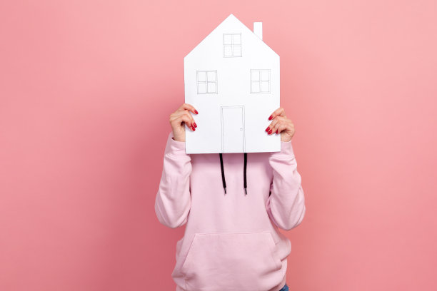 穿着连帽衫的年轻女子的肖像，脸上盖着大纸房子，梦想着自己的住所图片下载