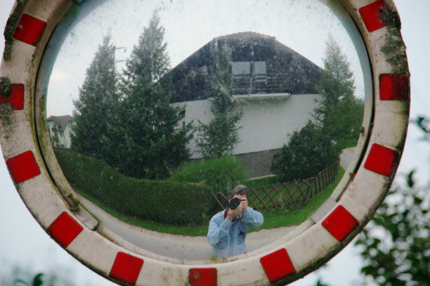 街头摄影师在肮脏的室外镜子里拍摄自己和身后的房子。图片下载