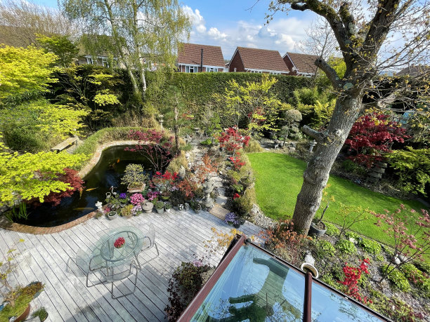 阳光明媚的夏日后花园，带凹槽的木制露台餐厅，玻璃露台桌子和有机玻璃椅子，盆栽树日本枫树展示，东方禅意植物和upvc玻璃屋顶温室图片下载