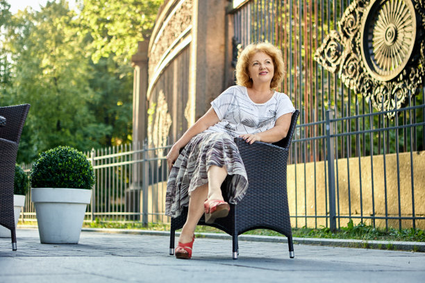 一个50岁的女人坐在路边咖啡馆旁边的椅子上。图片下载