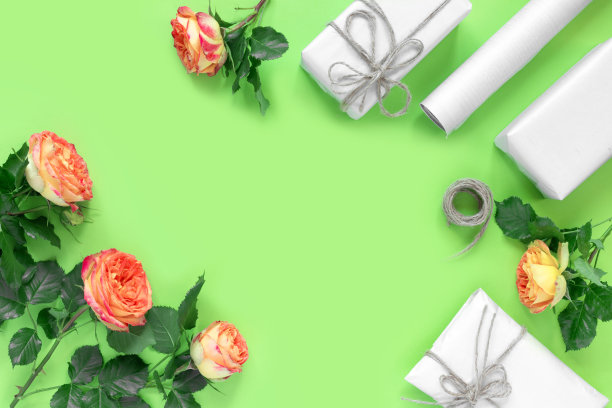 绿色背景中用绳子绑着的包装纸礼品盒和红黄色玫瑰花束图片下载