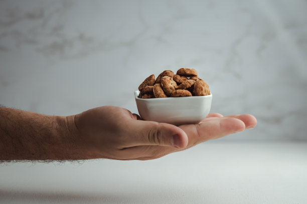 手拿着一个陶瓷碗，里面装满了巧克力曲奇饼，背景是精致的白色。极简主义的食物照片图片下载