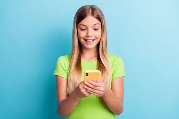 照片年轻开朗积极好心情女孩沉迷于社交网络使用智能手机孤立在蓝色背景图片下载