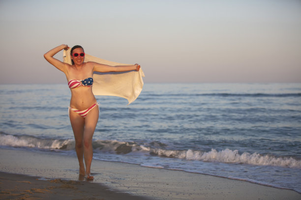 一位中年妇女穿着印有美国国旗的泳装沿着海岸走着。图片下载