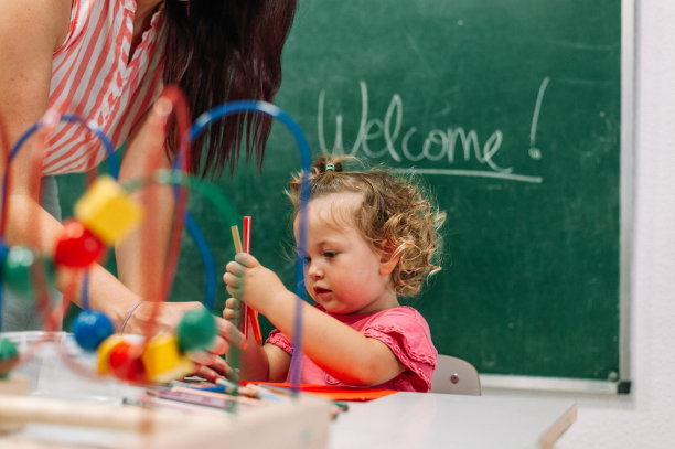 老师和学步的小女孩在幼儿园用彩色铅笔画画照片图片下载