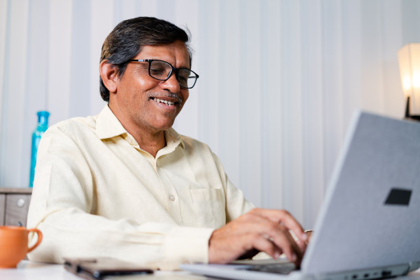 商人在工作时微笑或在办公室用笔记本电脑聊天的低角度视角-利用科技，沟通和互联网的概念图片下载