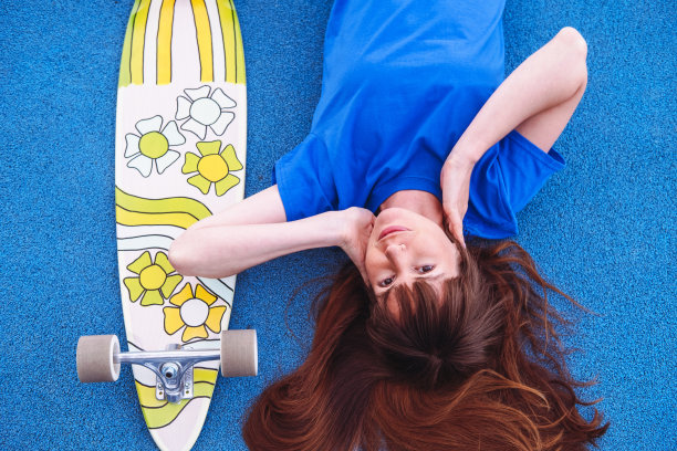 年轻妇女的肖像与滑板在蓝色的背景。女人穿蓝色t恤。图片下载