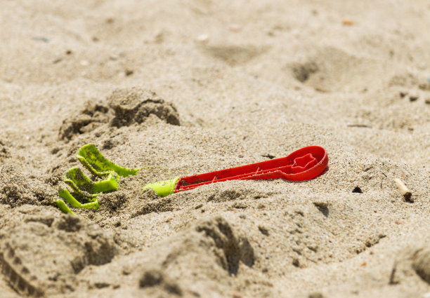 孩子们在沙滩上玩的红绿塑料耙子图片下载