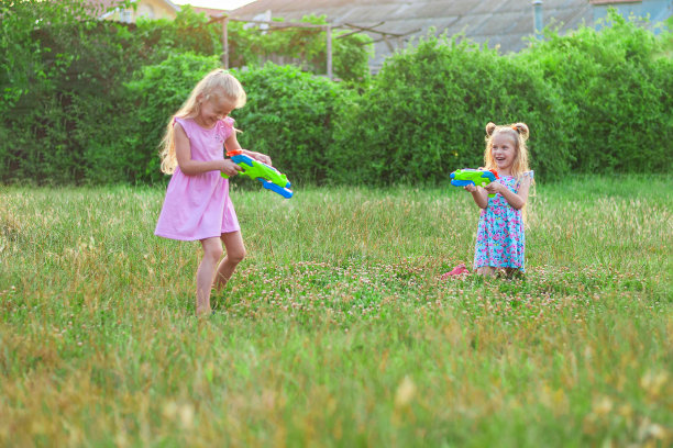夏天，两个小女孩拿着水枪在绿色的草地上玩耍图片下载