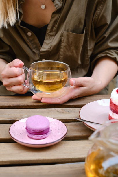 一个女人手里拿着一杯茶，坐在咖啡馆的夏日露台上，吃着甜杏仁甜点和一块红色天鹅绒蛋糕。美味的法式甜点马卡龙和美式红丝绒蛋糕图片下载