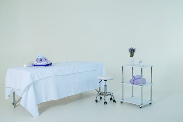 按摩沙发盖着白色毛巾布床单。椅子、桌子、毛巾、蜡烛和一个插着薰衣草的花瓶。都在白色的背景上。图片下载