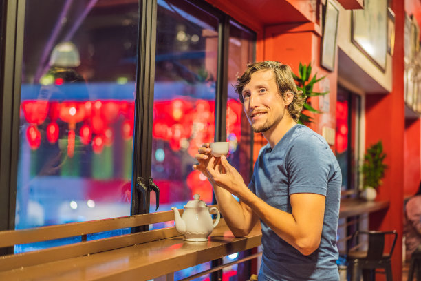 为了庆祝中国新年，一名年轻人在红灯笼的背景下喝着中国茶图片下载