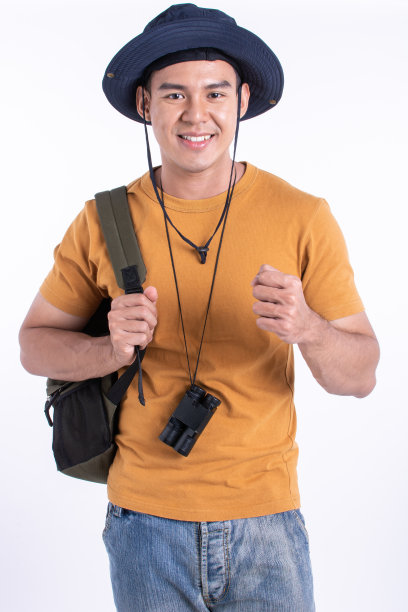 英俊的亚洲男游客戴着帽子，穿着休闲的衣服，牛仔裤带着相机，夏天旅行背包，摆着姿势，看着相机，幸福的微笑，站在孤立的白色背景剪纸。图片下载