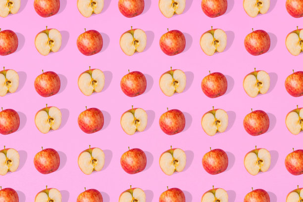新鲜的苹果和苹果的一半在粉红色的背景上突出的图案。图片下载