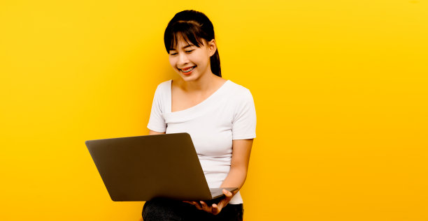 亚洲女性程序员美丽的商人女人的肖像兴奋的亚洲女孩拿着笔记本电脑和庆祝成功在黄色背景图片下载