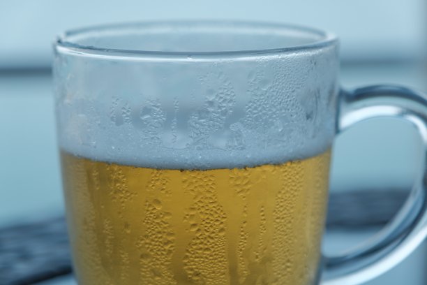 淡啤酒。冷饮啤酒，杯中满是啤酒滴。桌上放着一杯啤酒，背景是平静的大海图片下载