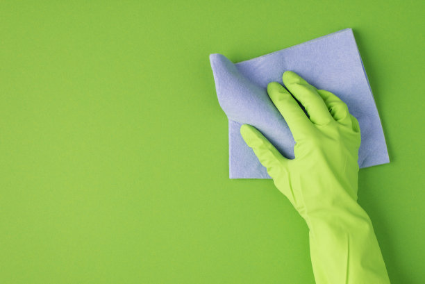 俯视图照片的手在绿色橡胶手套擦拭表面与紫丁香抹布孤立的绿色背景与copyspace在左边图片下载