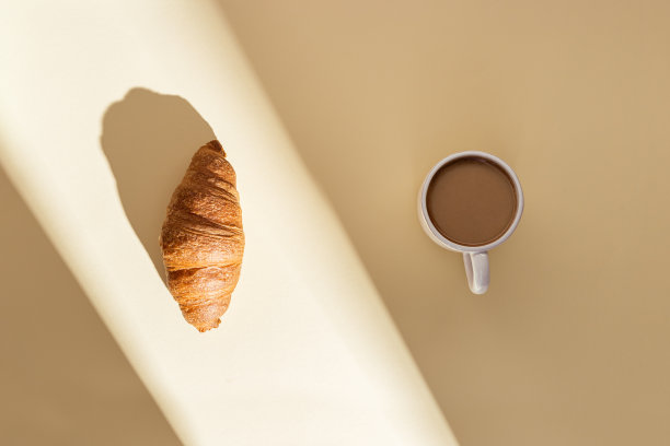 美味的牛角面包和一杯牛奶咖啡，米色的阳光。阳光明媚的夏日早餐。图片下载