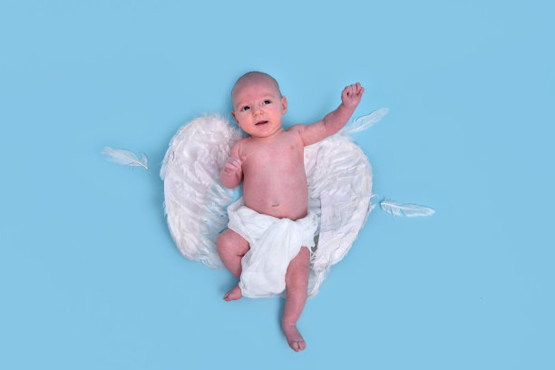 一个有着白色天使翅膀的新生男婴在一个蓝色背景的工作室里，复印空间。一个穿着尿布的白人婴儿一个月大图片下载