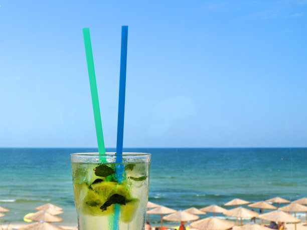 一杯莫吉托鸡尾酒，用吸管在地平线和海滩的背景下图片下载