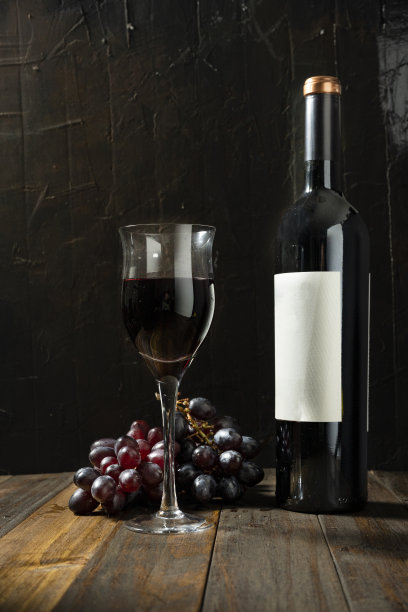 在一张质朴的木桌和深色背景上，满杯的红酒旁边放着一瓶红酒。图片下载