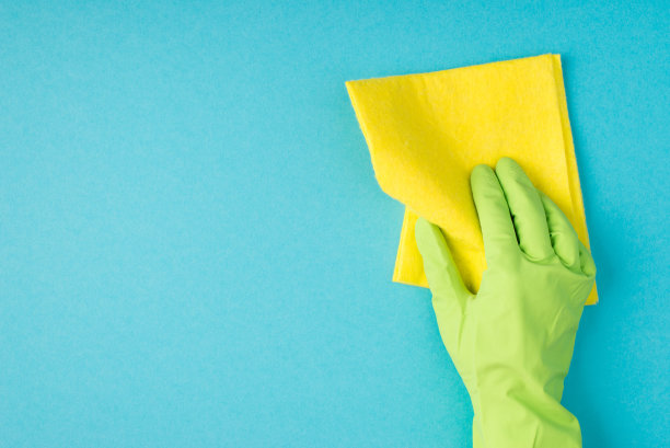 顶视图照片的手在绿色橡胶手套持有黄色粘胶抹布上孤立的淡蓝色背景与copyspace图片下载