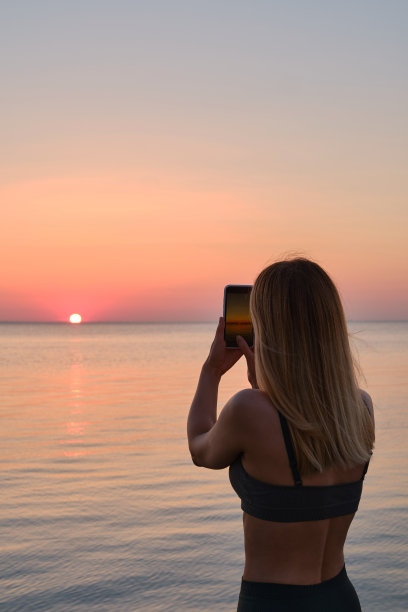女孩手里拿着手机，在黎明时分拍下了大海的照片。专注于手机屏幕。用你的智能手机制造记忆。手机特写图片下载