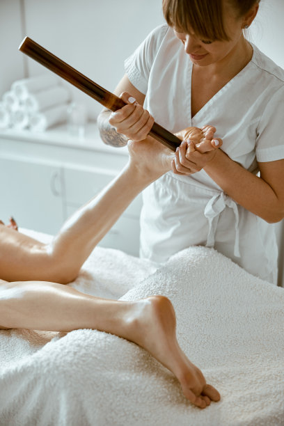 自信的女性专家正在用竹签给美丽的高加索女性客户做腿部按摩图片下载