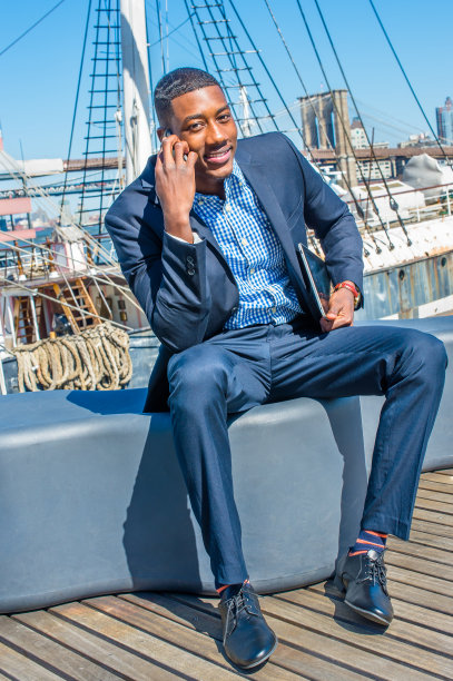 一名年轻的黑人男子坐在纽约市河边的户外，正在讲手机图片下载