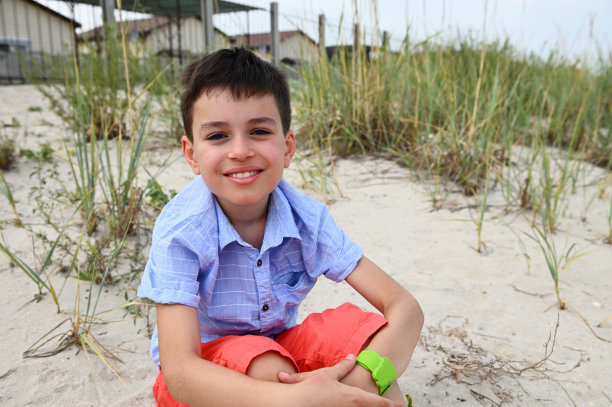 在大自然的映衬下，一个英俊的孩子以莲花的姿势坐在沙滩上，微笑着看着镜头。放松，宁静和健康的概念。图片下载