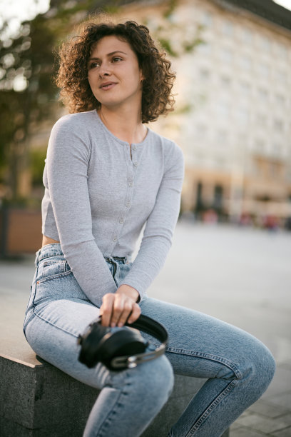 一个年轻快乐的女人正坐在城市广场上瑟瑟发抖。这个女人手里拿着耳机。图片下载