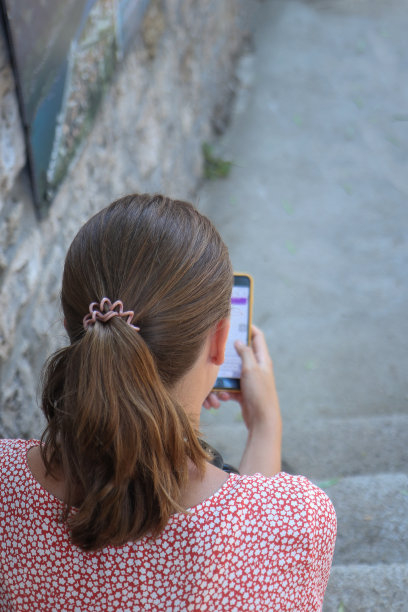 一个年轻的女人坐在楼梯上使用手机在古老的地中海小镇图片下载