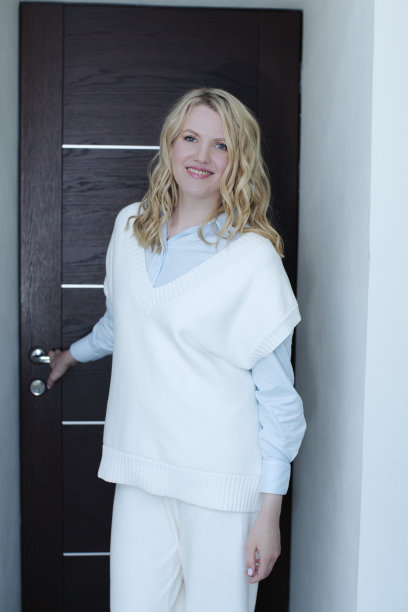 穿着白色毛衣的金发美女微笑着对着办公室敞开的门，邀请、会见和送别客人图片下载