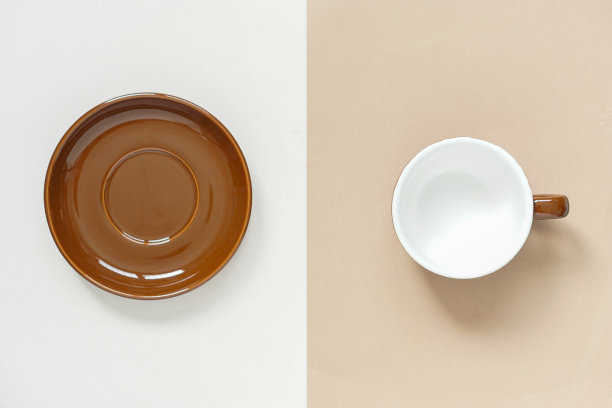 空的棕色圆形陶瓷杯和棕色圆形陶瓷碟放置在奶油和棕色的背景与柔和的光线在早上，概念的陶瓷模型为广告。图片下载