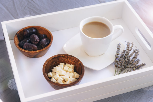 一杯咖啡，椰子块，枣子水果和薰衣草花放在床上的木制托盘上。健康的早餐。俯视图图片下载