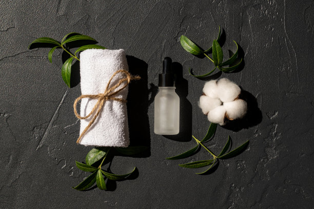 精油或面部精华液与白色毛巾和棉花花在黑色背景。有机化妆品。水疗美容护肤、保健。品牌商业。产品照片。模板图片下载