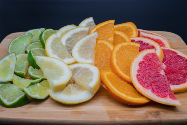 将酸橙、柠檬、橘子和葡萄柚片放在黑色背景的切菜板上。热带图片与各种切片柑橘类水果。图片下载
