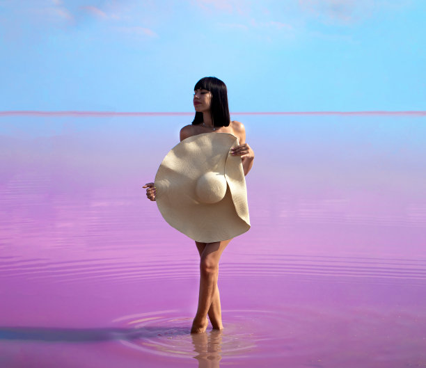 一个手里拿着帽子的女孩站在淡紫色的盐湖上，映衬着蓝色的天空图片下载