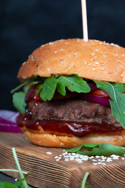 美味多汁的汉堡，由牛肉、香草和蔬菜做成，放在黑色背景的木板上。高脂肪垃圾食品的特写镜头。照片为菜单或海报。快餐的概念。图片下载