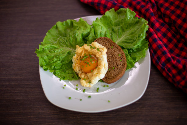 白盘子上的煎蛋，配上沙拉和面包的叶子，棕色的桌子和红色的纺织品图片下载