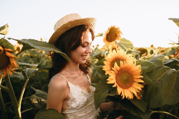 一个带着帽子微笑的女人站在夕阳下的向日葵地里图片下载
