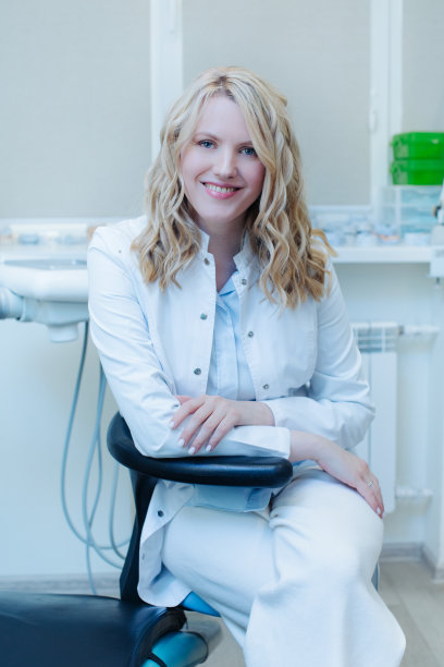 美丽的金发牙医微笑着快乐自信的样子坐在医生的牙科诊所。图片下载